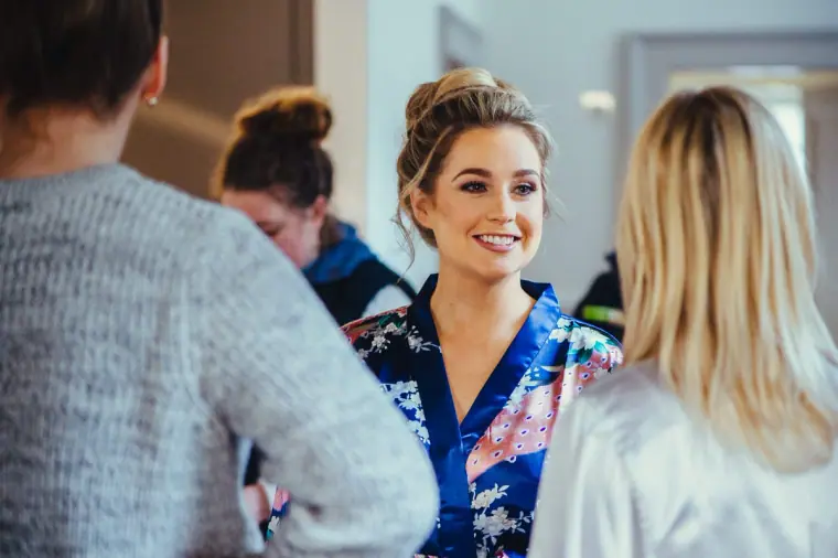 Smiling bride in a floral robe chatting with bridesmaids while getting ready