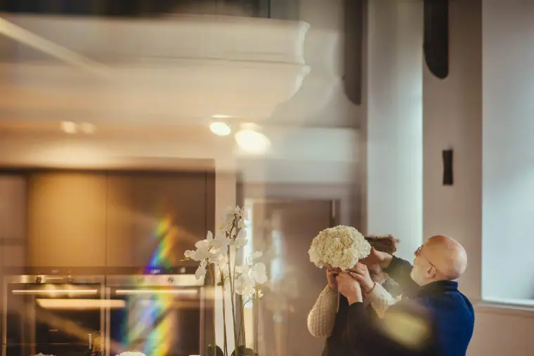 Florist arranging a white bouquet in a sunlit room, rainbow flare in the foreground