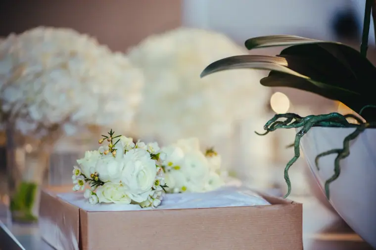White rose bouquets and buttonholes on a box beside an orchid
