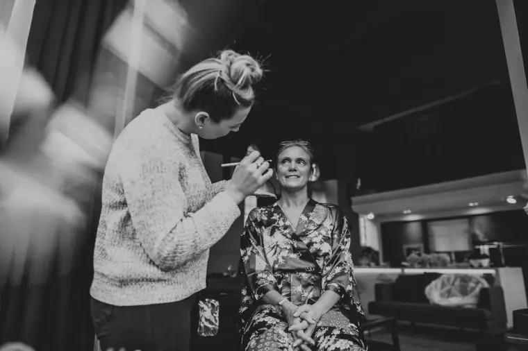 Black-and-white photo of a make-up artist working on a woman in a floral robe