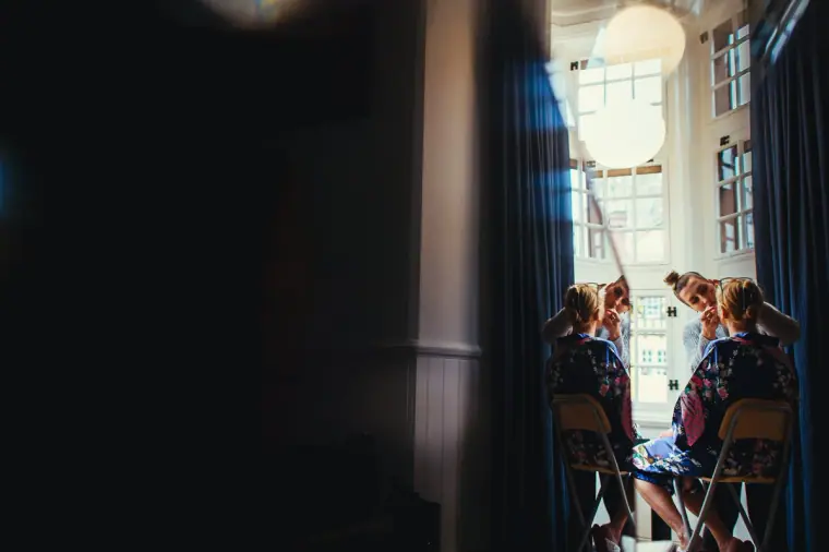 Bridesmaids in matching floral robes getting ready by a tall window