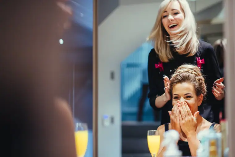 Bridesmaid laughing with her hands to her face as her hair is styled