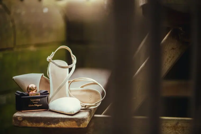 Bride's ivory heels and perfume bottle arranged on a wooden ledge