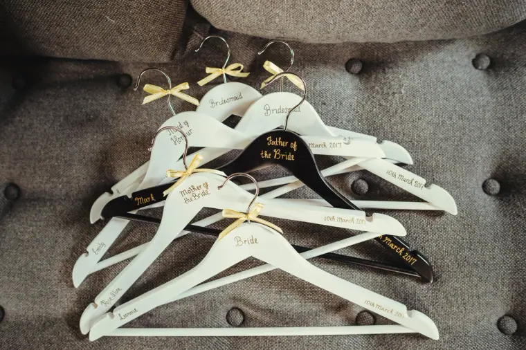 Personalised white wedding hangers with gold bows and names laid on a grey sofa