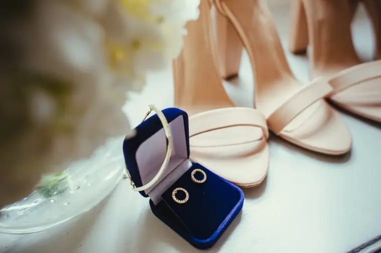 Earrings in a navy velvet box beside nude strappy heels