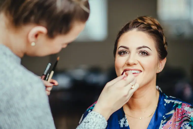 Bridesmaid smiling as her lipstick is applied by the make-up artist