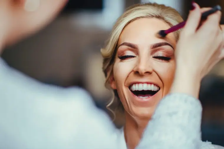 Laughing bridesmaid having eyeshadow applied with a brush