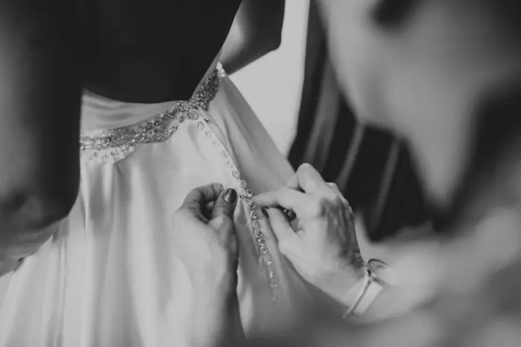 Black-and-white close-up of hands fastening the back of the wedding gown