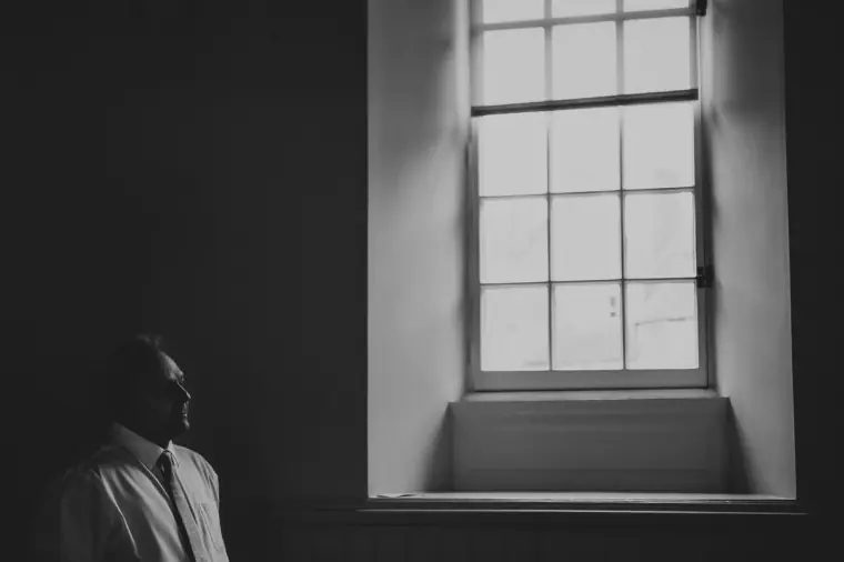 Black-and-white silhouette of a man waiting by a tall sash window