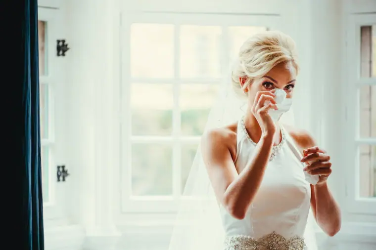 Emotional bride dabbing a tear in front of bright windows