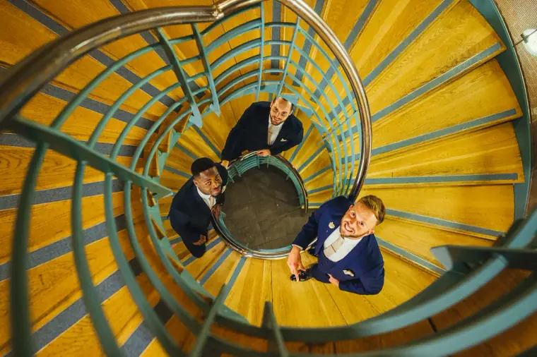 Groom and groomsmen looking up from the bottom of a yellow spiral staircase