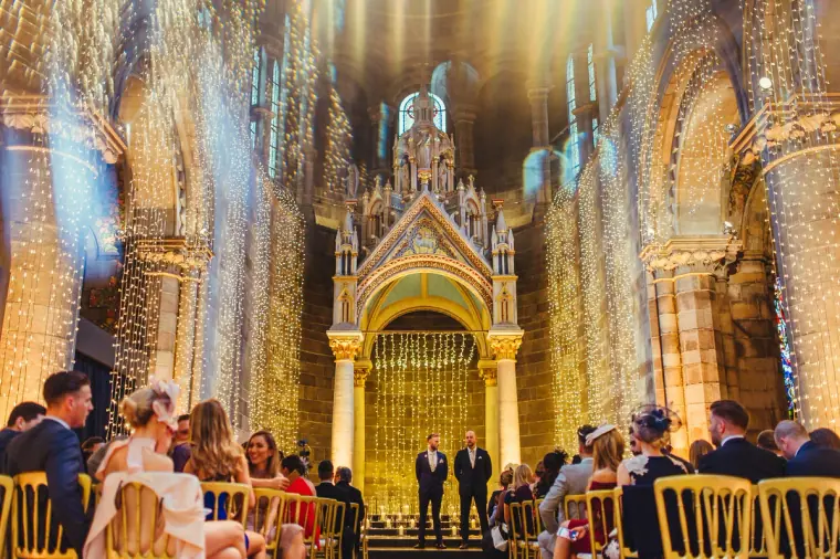 Guests seated in Mansfield Traquair's golden nave as the groom waits at the altar