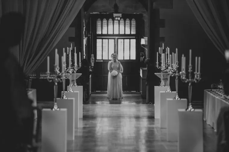 Black-and-white photo of a bridesmaid at the end of the candelabra-lined aisle
