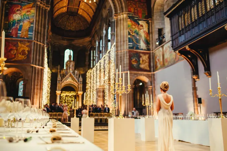 Bridesmaid walking past long tables beneath Mansfield Traquair's painted murals