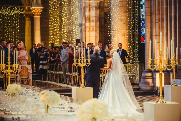 Bride reaching the groom at the front of the candlelit hall, guests watching