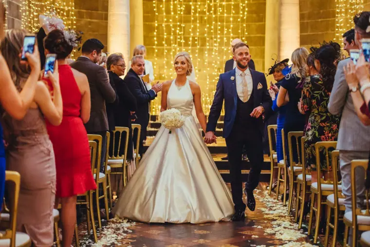 Newlyweds walking back down the aisle as guests photograph them
