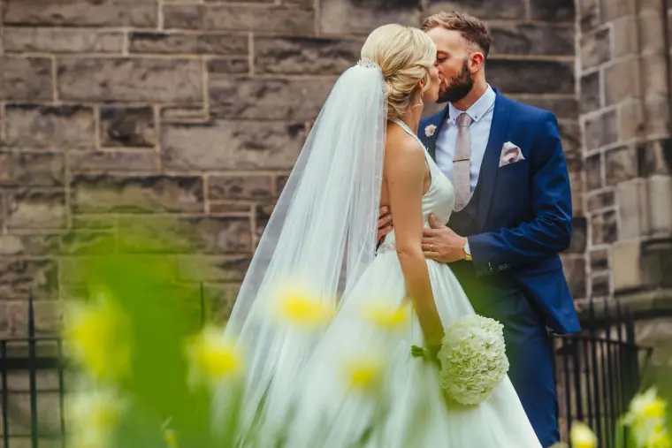 Andy kissing Leonnie beside the stone wall, daffodils blurred in the foreground