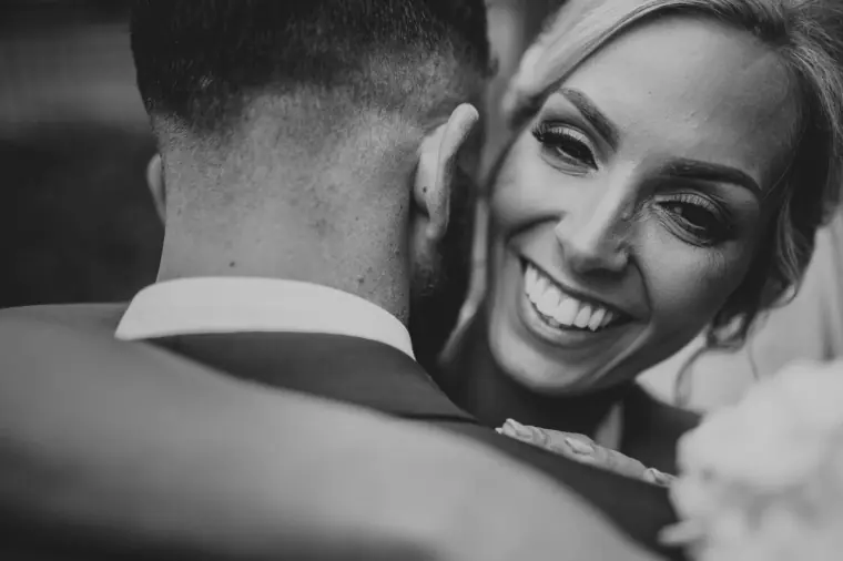 Black-and-white close-up of the bride beaming as she hugs the groom