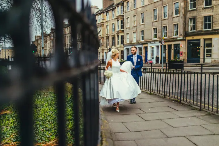 Groom carrying the bride's veil as she walks along an Edinburgh street