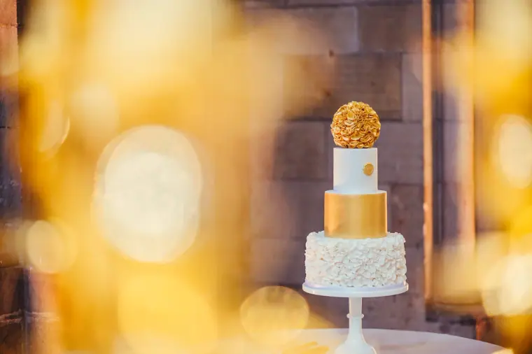White ruffled wedding cake topped with gold tiers and a gold flower ball