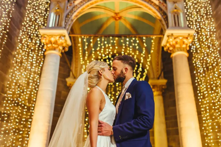 Leonnie and Andy kissing beneath a gilded arch hung with fairy lights