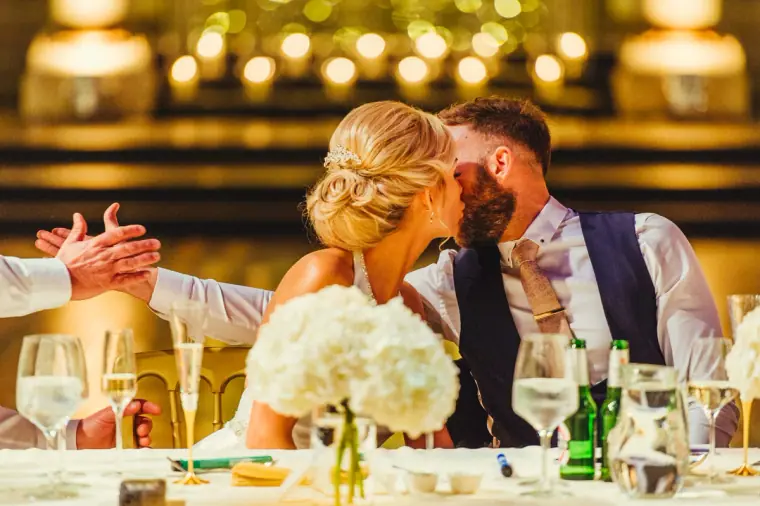 Leonnie kissing Andy at the top table as a guest reaches out to shake his hand