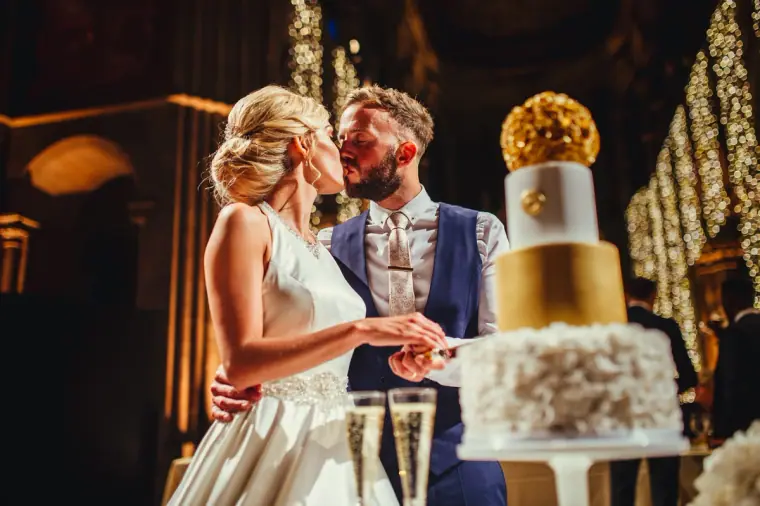 Leonnie and Andy kissing as they cut their gold-tiered wedding cake