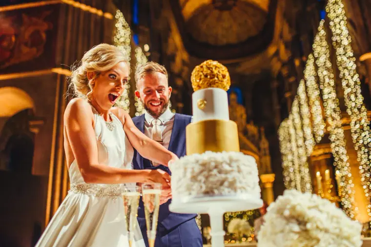 Bride laughing as the couple cut the cake beneath curtains of fairy lights