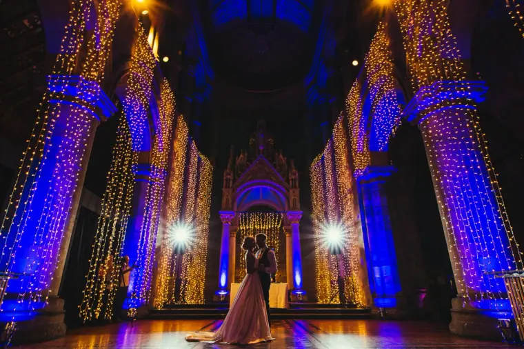 Couple's first dance at the end of the hall, pillars lit in blue and gold