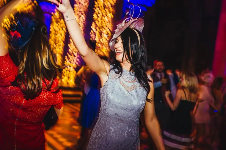 Guest in a fascinator dancing with arms raised on the dance floor