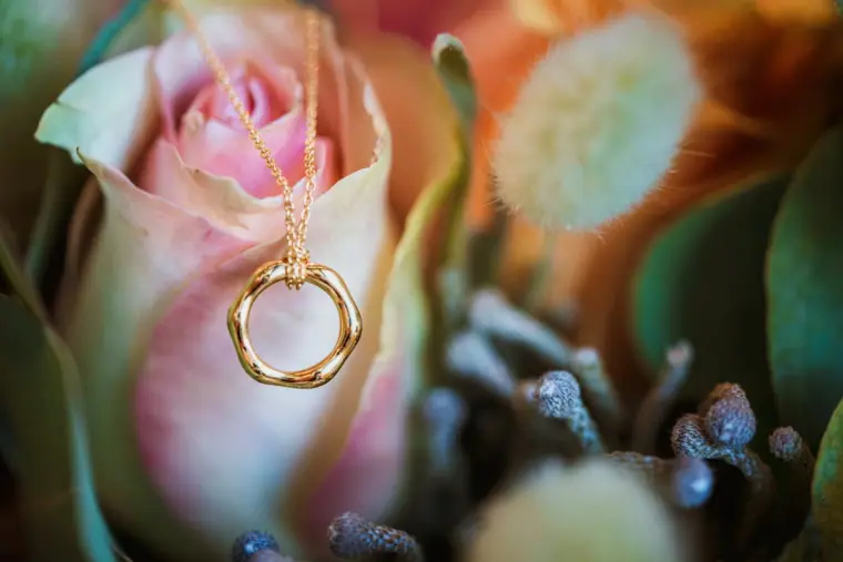 Gold pendant necklace resting on a pink rose in a bouquet