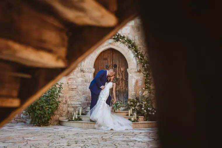 Couple embracing by an arched wooden door, framed through a staircase