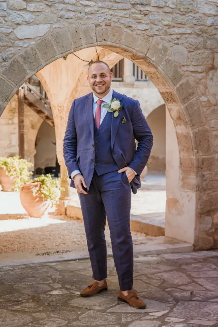 Groom in a navy three-piece suit standing beneath a stone arch