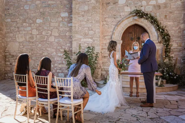 Emily and Chris saying their vows before a few guests at the stone chapel door
