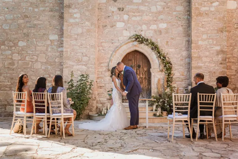 Emily and Chris kissing at the chapel door as their few guests watch
