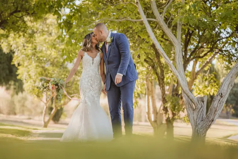 Emily and Chris kissing on a tree-lined path in golden light
