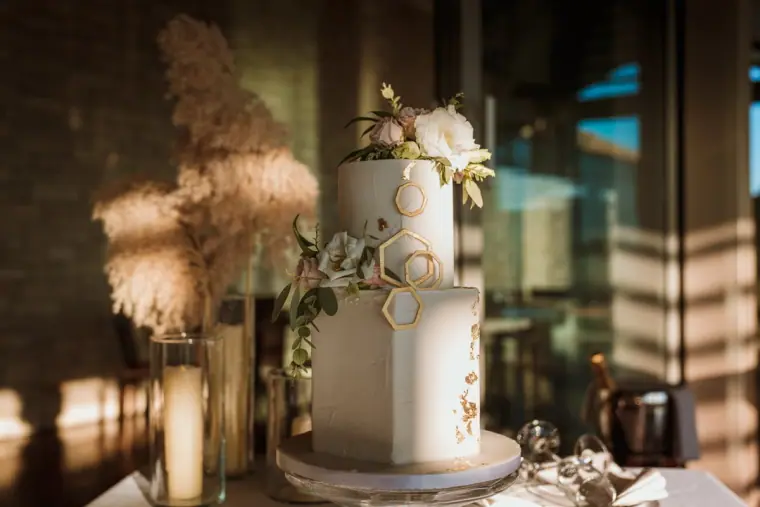 Two-tier white wedding cake with flowers and pampas grass in warm window light