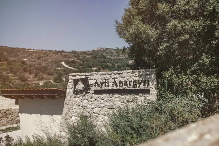Stone entrance sign for Ayii Anargyri set against wooded hills