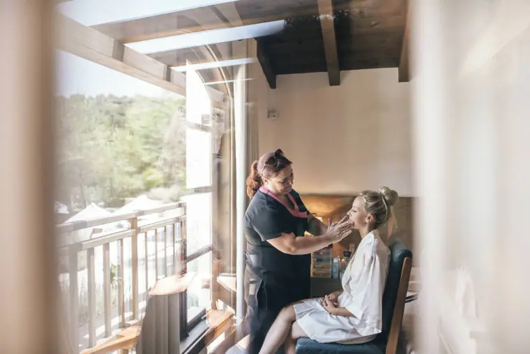 Bride having her make-up done by a balcony door in a beamed hotel room