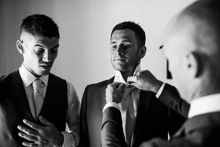 Black-and-white photo of groomsmen adjusting the groom's tie