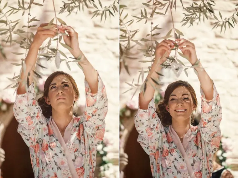 Bridesmaid in a floral robe hanging decorations in an olive tree