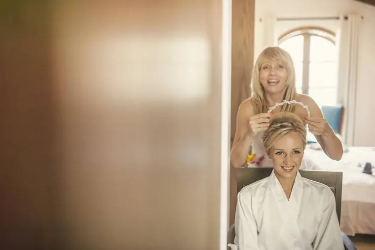 Bride in a white robe smiling as her hair is styled