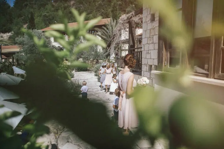 Bridesmaids walking along a garden path to the ceremony, framed by leaves