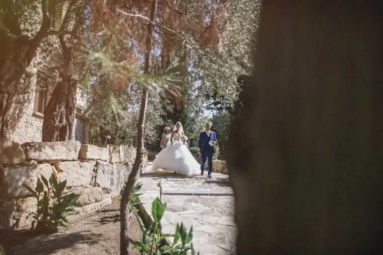 Bride and her father walking down a stone path under olive trees
