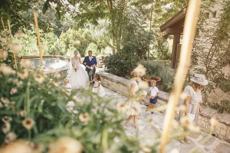 Bride on her father's arm walking down the garden aisle as guests watch