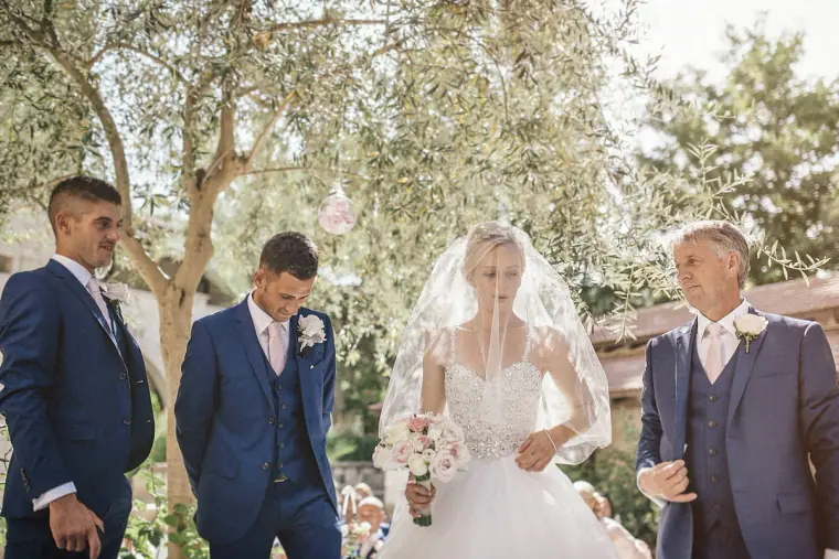 Emmee arriving beside Danny and the groomsmen under olive trees