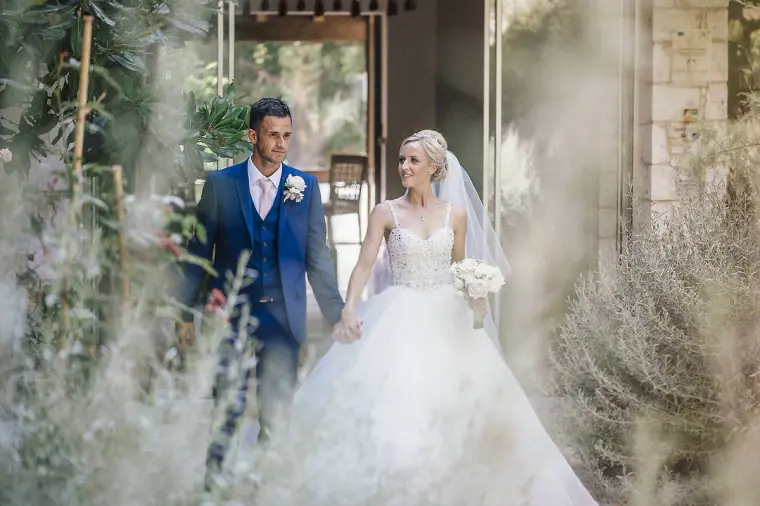 Bride and groom walking through a garden of silvery herbs at Ayii Anargyri