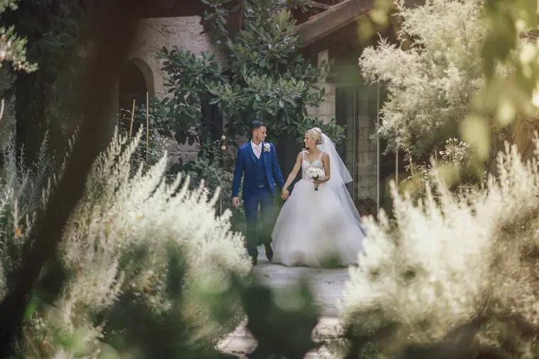 Emmee and Danny strolling together between flowering shrubs