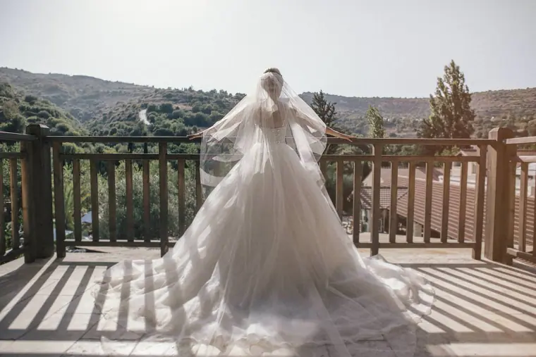 Bride's full gown and long veil spread across a sunlit wooden balcony overlooking hills