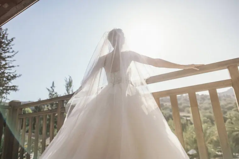 Bride from behind with arms outstretched, veil glowing in the sun on the balcony